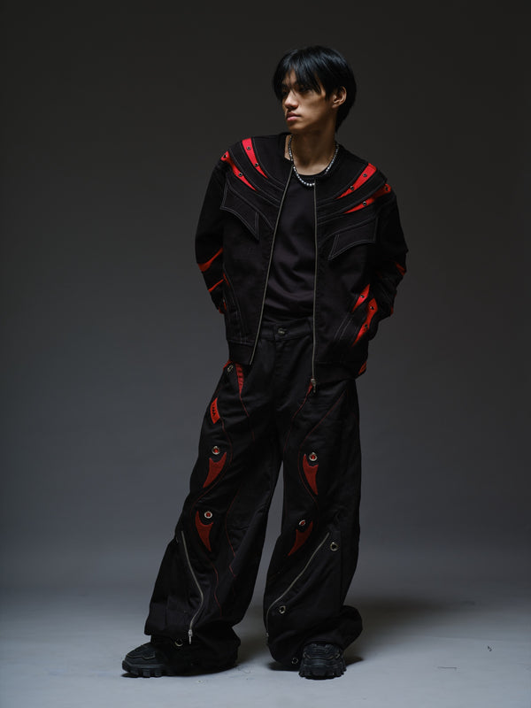 Black baggy denim pants with red patches beneath black net, oversized metal eyelets and large lower-leg zipper pockets