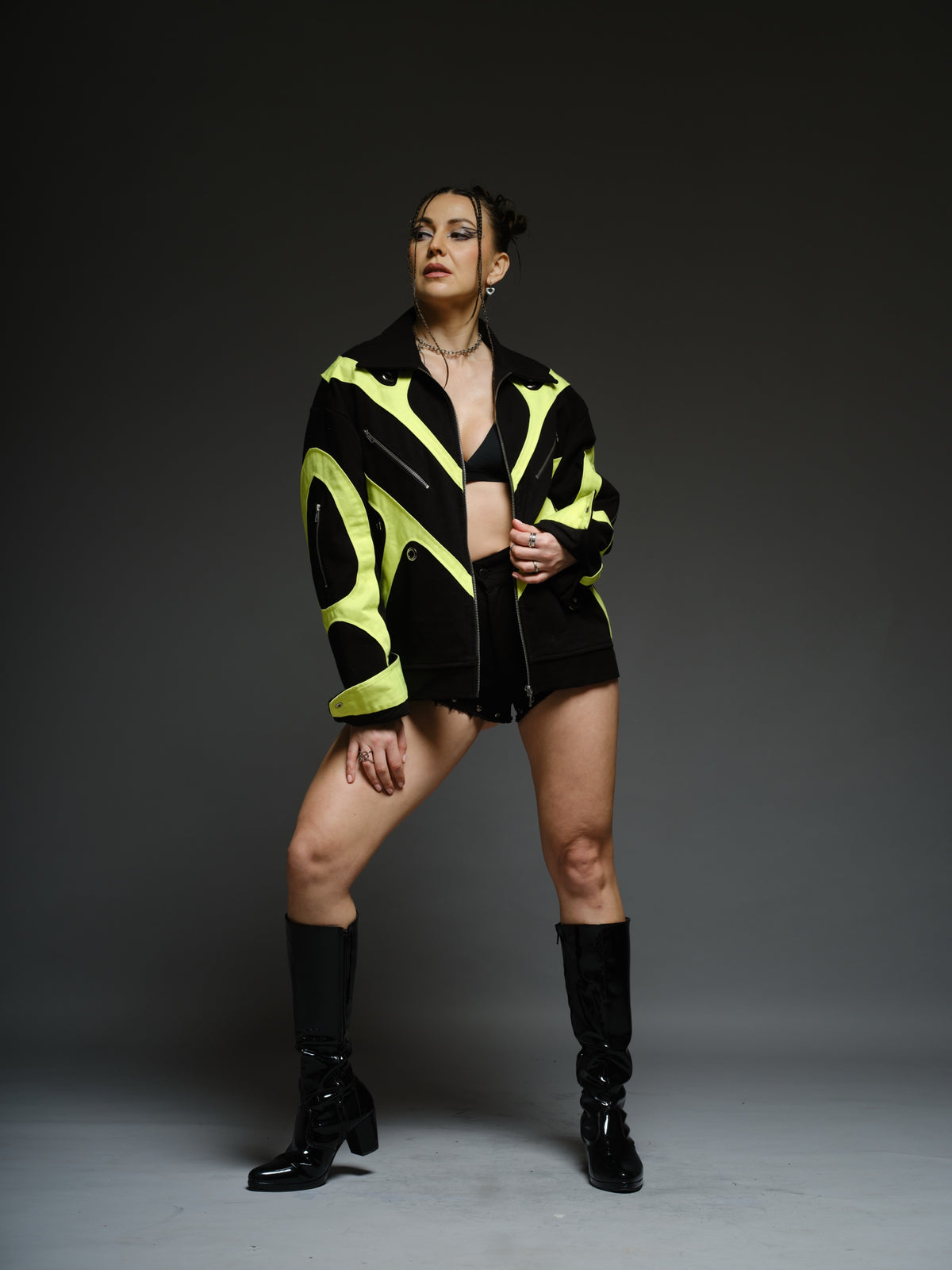 Black denim jacket with neon panels across the chest and sleeves, decorative silver zippers, large metal eyelets and a broad collar.