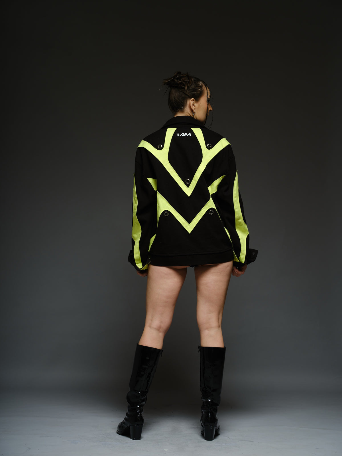 Black denim jacket with neon panels across the chest and sleeves, decorative silver zippers, large metal eyelets and a broad collar.