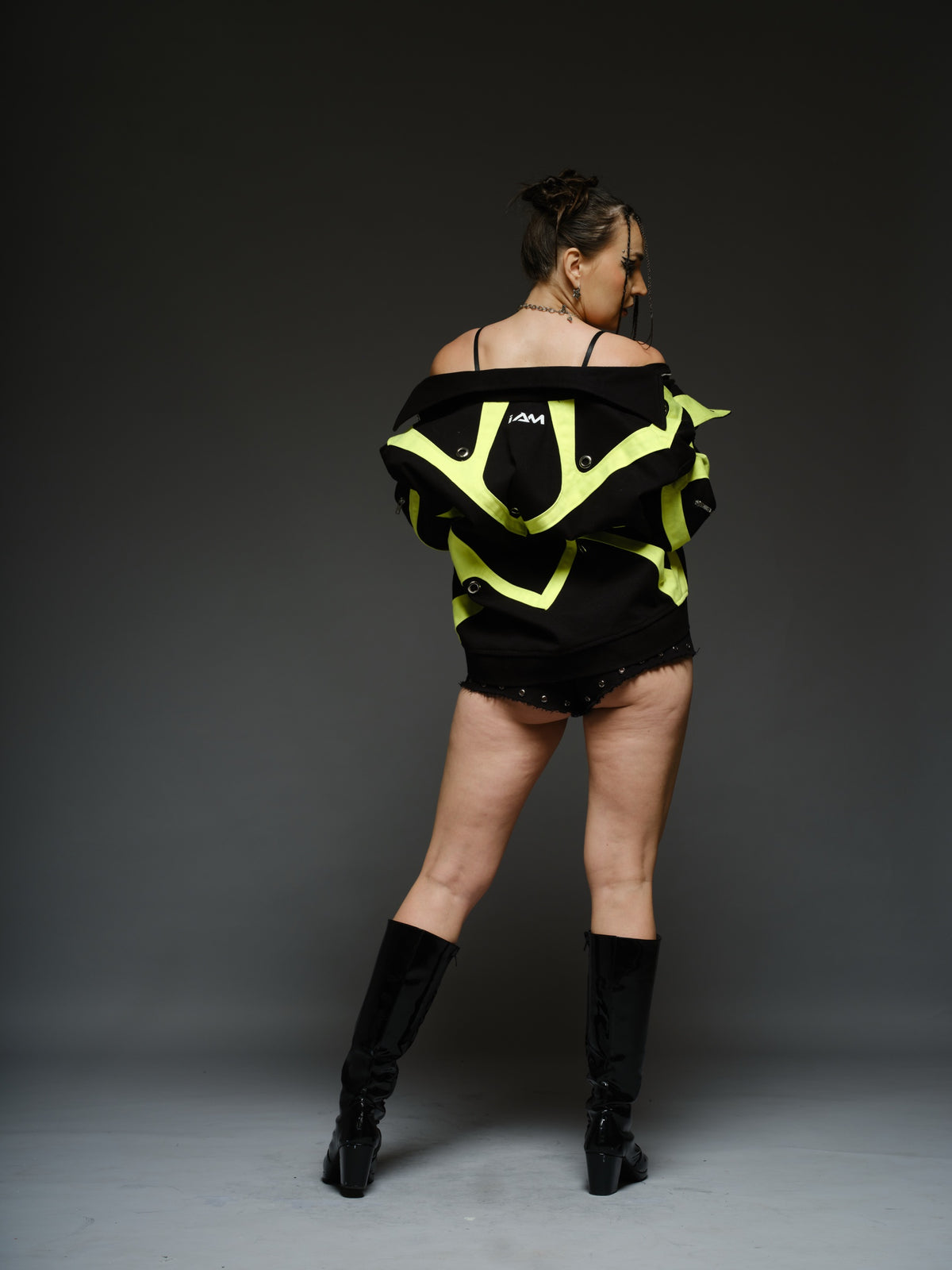 Black denim jacket with neon panels across the chest and sleeves, decorative silver zippers, large metal eyelets and a broad collar.