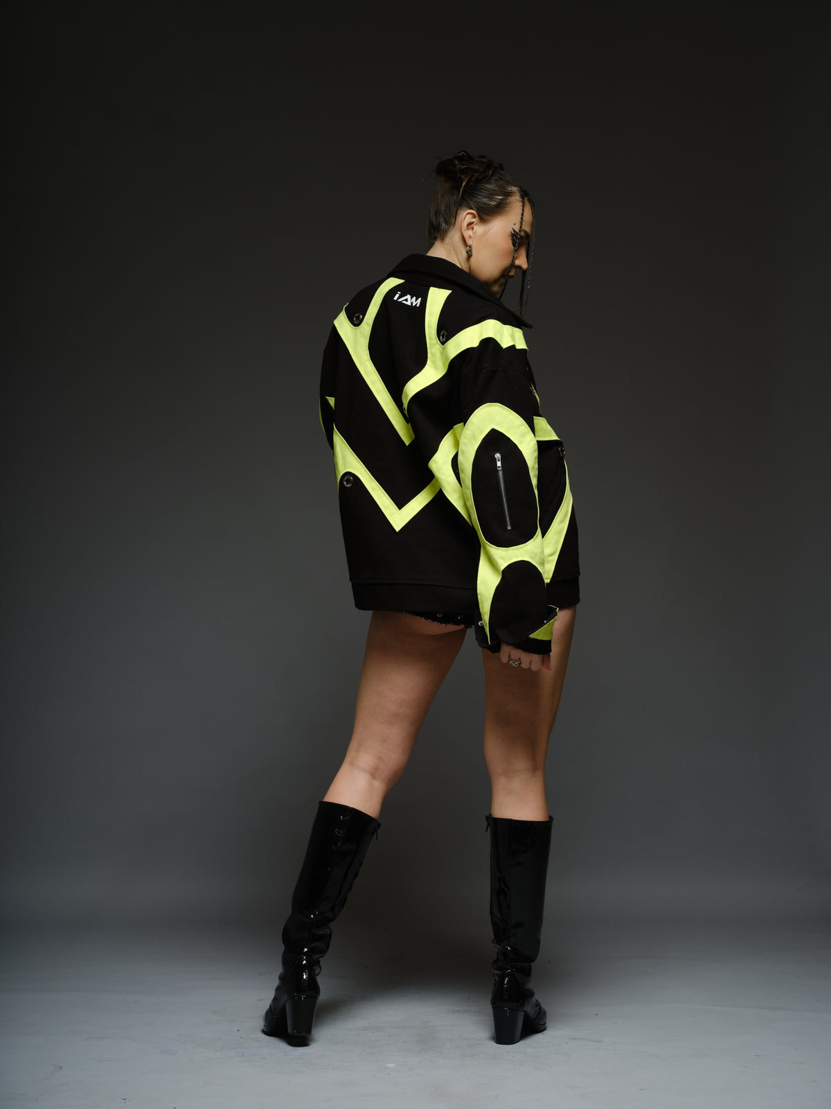 Black denim jacket with neon panels across the chest and sleeves, decorative silver zippers, large metal eyelets and a broad collar.