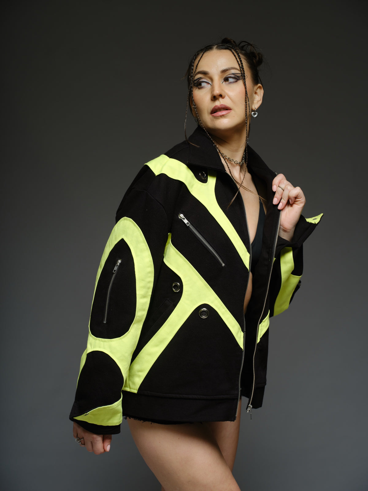 Black denim jacket with neon panels across the chest and sleeves, decorative silver zippers, large metal eyelets and a broad collar.