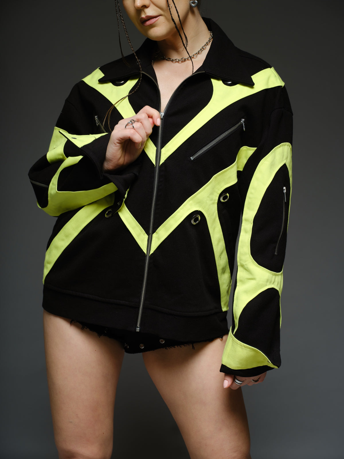 Black denim jacket with neon panels across the chest and sleeves, decorative silver zippers, large metal eyelets and a broad collar.