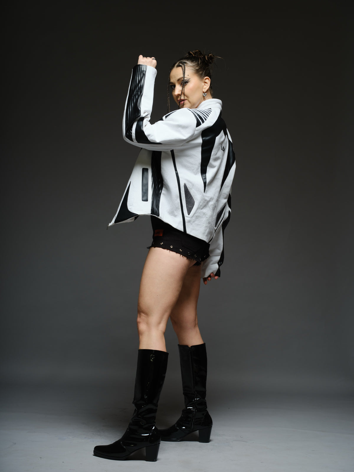 White denim jacket with curved black leather patches, white cord detailing across black shoulders, vertical chest zippers and zipped sleeves.