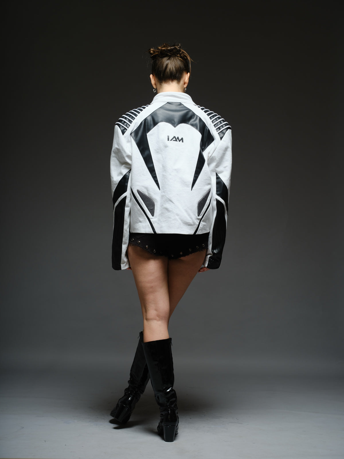 White denim jacket with curved black leather patches, white cord detailing across black shoulders, vertical chest zippers and zipped sleeves.