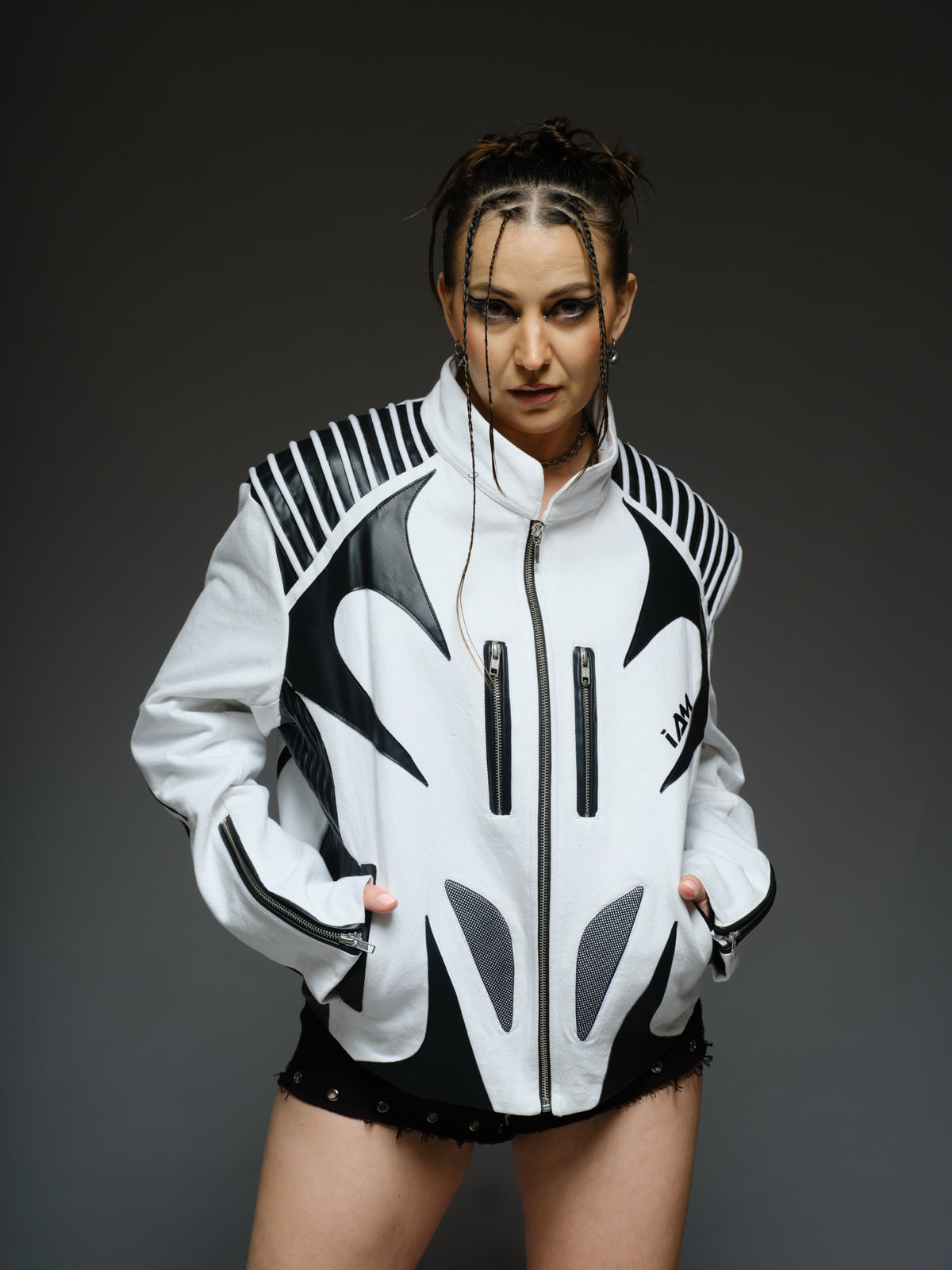White denim jacket with curved black leather patches, white cord detailing across black shoulders, vertical chest zippers and zipped sleeves.