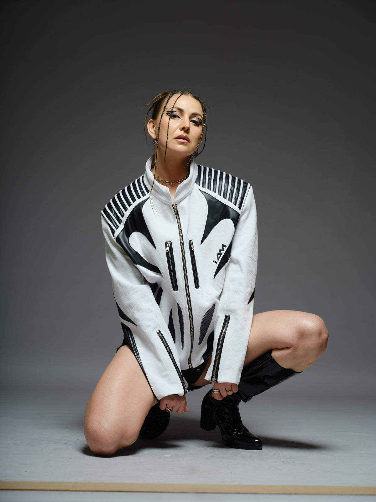 White denim jacket with curved black leather patches, white cord detailing across black shoulders, vertical chest zippers and zipped sleeves.