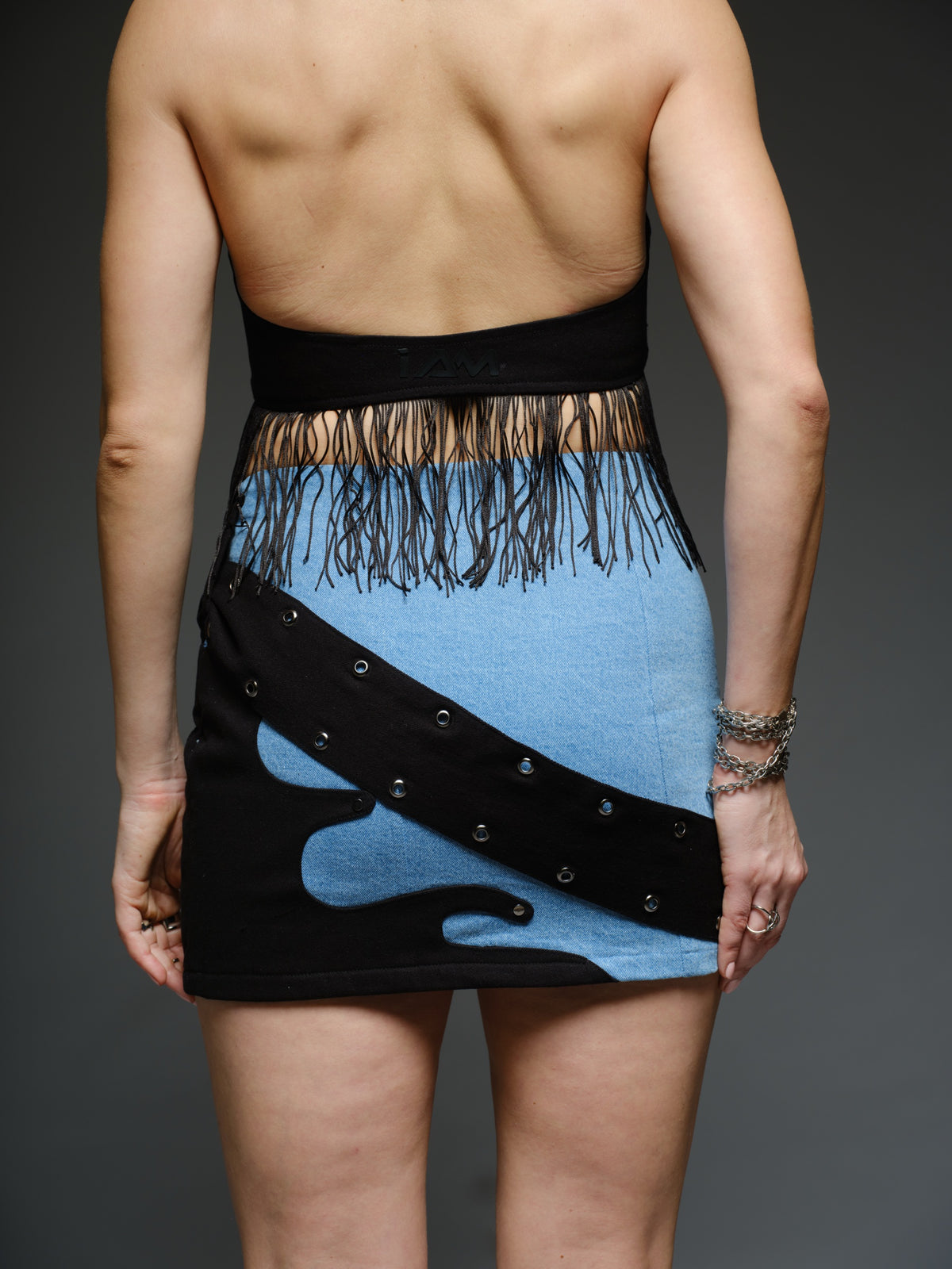 Black denim lace-up halter top with blue flame patches and fringe, paired with a blue denim mini skirt with black patches and diagonal buckle detailing