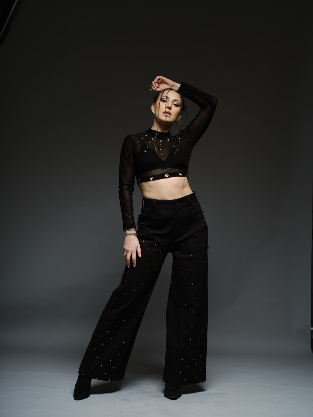 Black high-neck velvet mesh crop top with metallic rivets, paired with wide-leg black denim pants with silver-tone studs