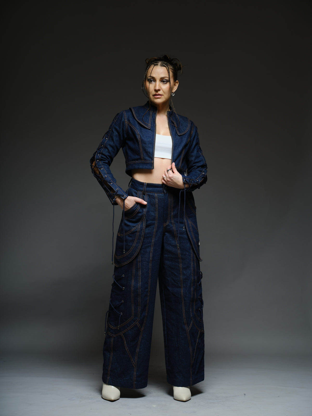 Indigo Set cropped denim jacket with oversized collar and lace-up sleeves, paired with panelled straight-leg pants with orange stitching
