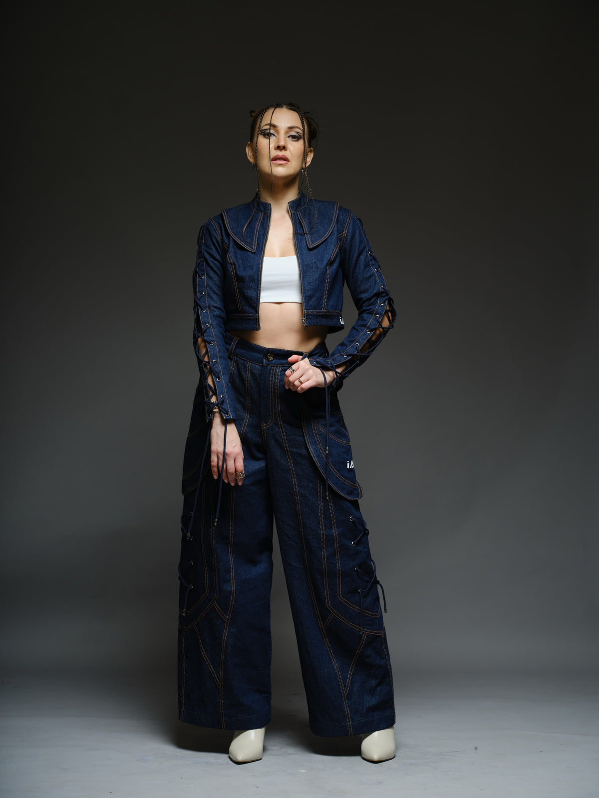 Indigo Set cropped denim jacket with oversized collar and lace-up sleeves, paired with panelled straight-leg pants with orange stitching