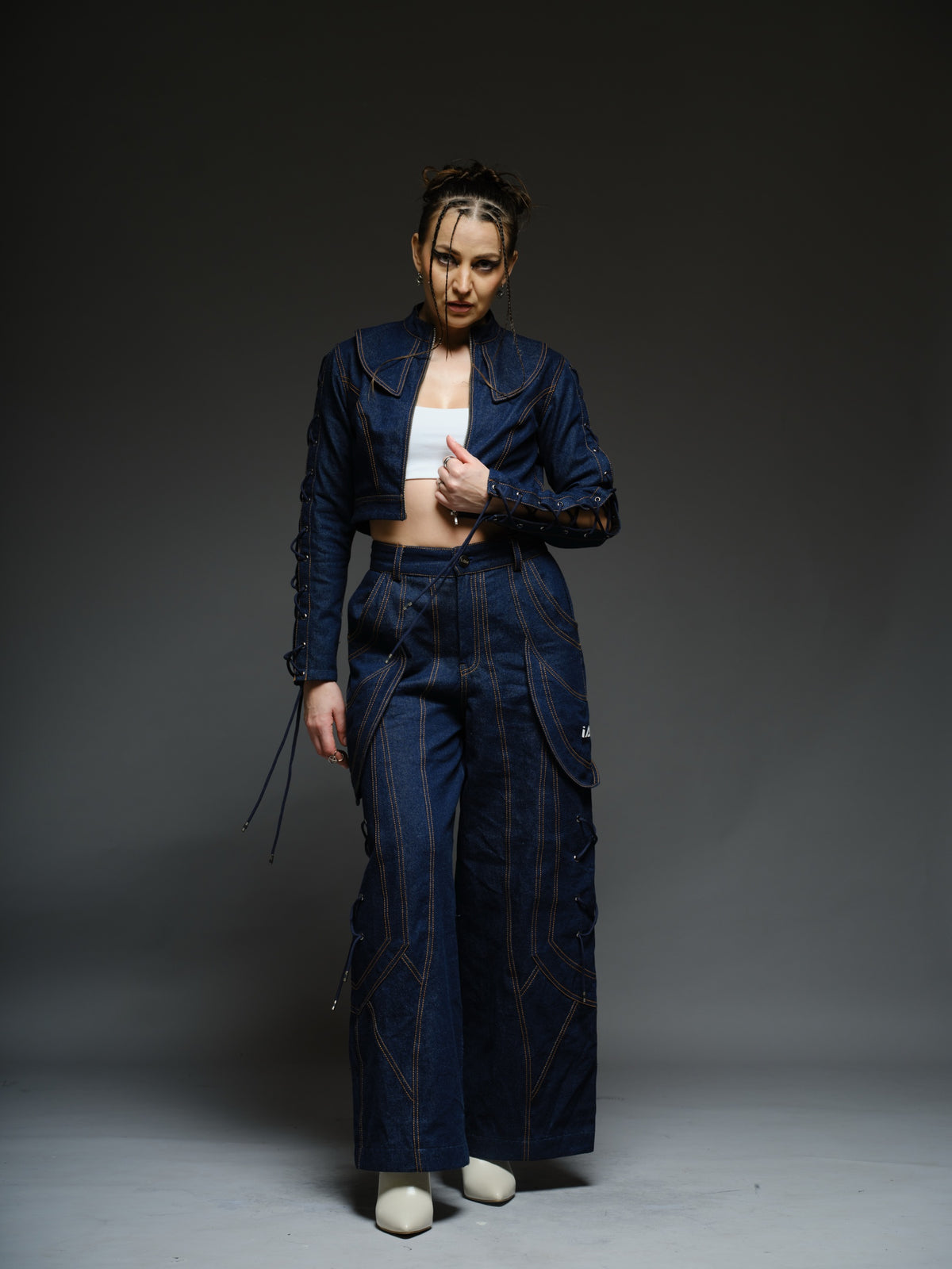 Indigo Set cropped denim jacket with oversized collar and lace-up sleeves, paired with panelled straight-leg pants with orange stitching