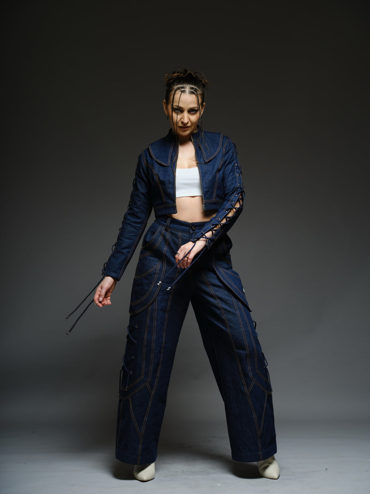 Indigo Set cropped denim jacket with oversized collar and lace-up sleeves, paired with panelled straight-leg pants with orange stitching