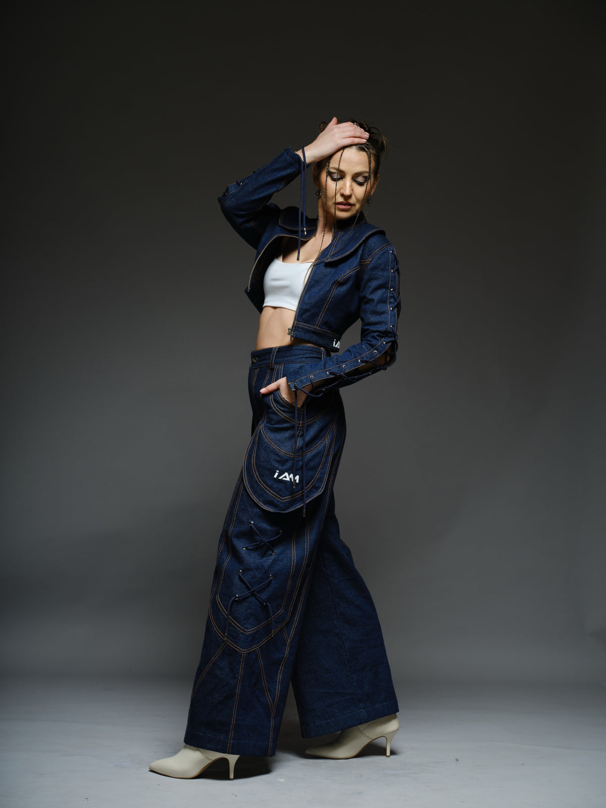 Indigo Set cropped denim jacket with oversized collar and lace-up sleeves, paired with panelled straight-leg pants with orange stitching