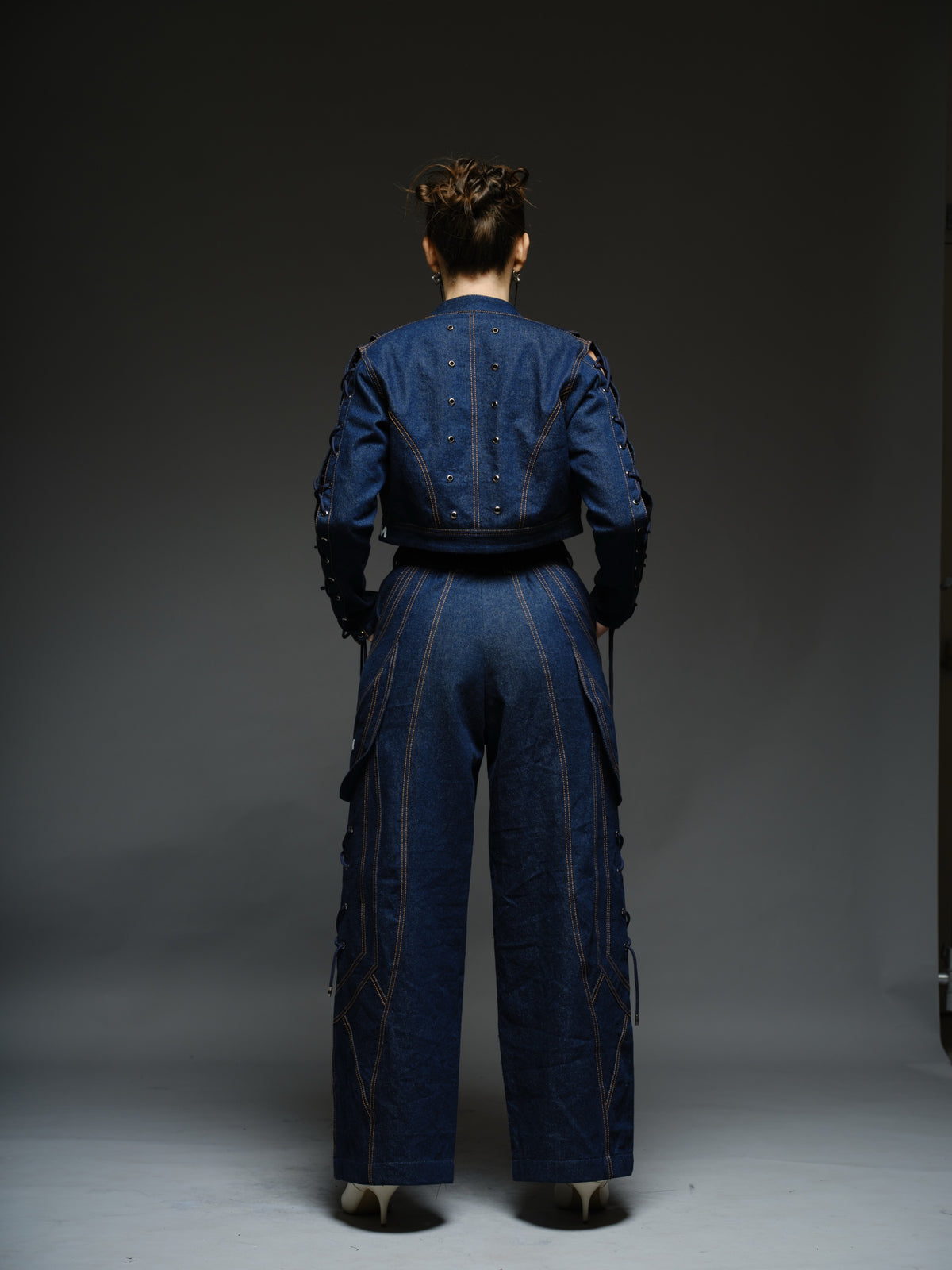 Indigo Set cropped denim jacket with oversized collar and lace-up sleeves, paired with panelled straight-leg pants with orange stitching