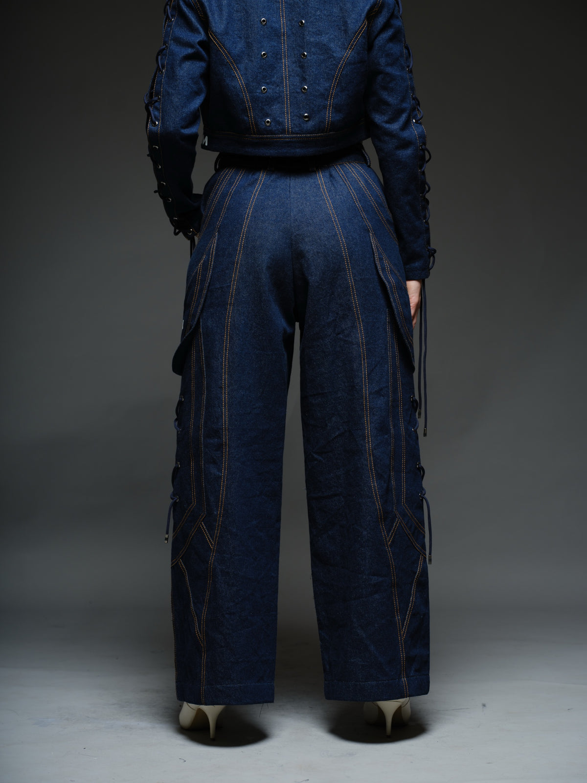 Indigo Set cropped denim jacket with oversized collar and lace-up sleeves, paired with panelled straight-leg pants with orange stitching
