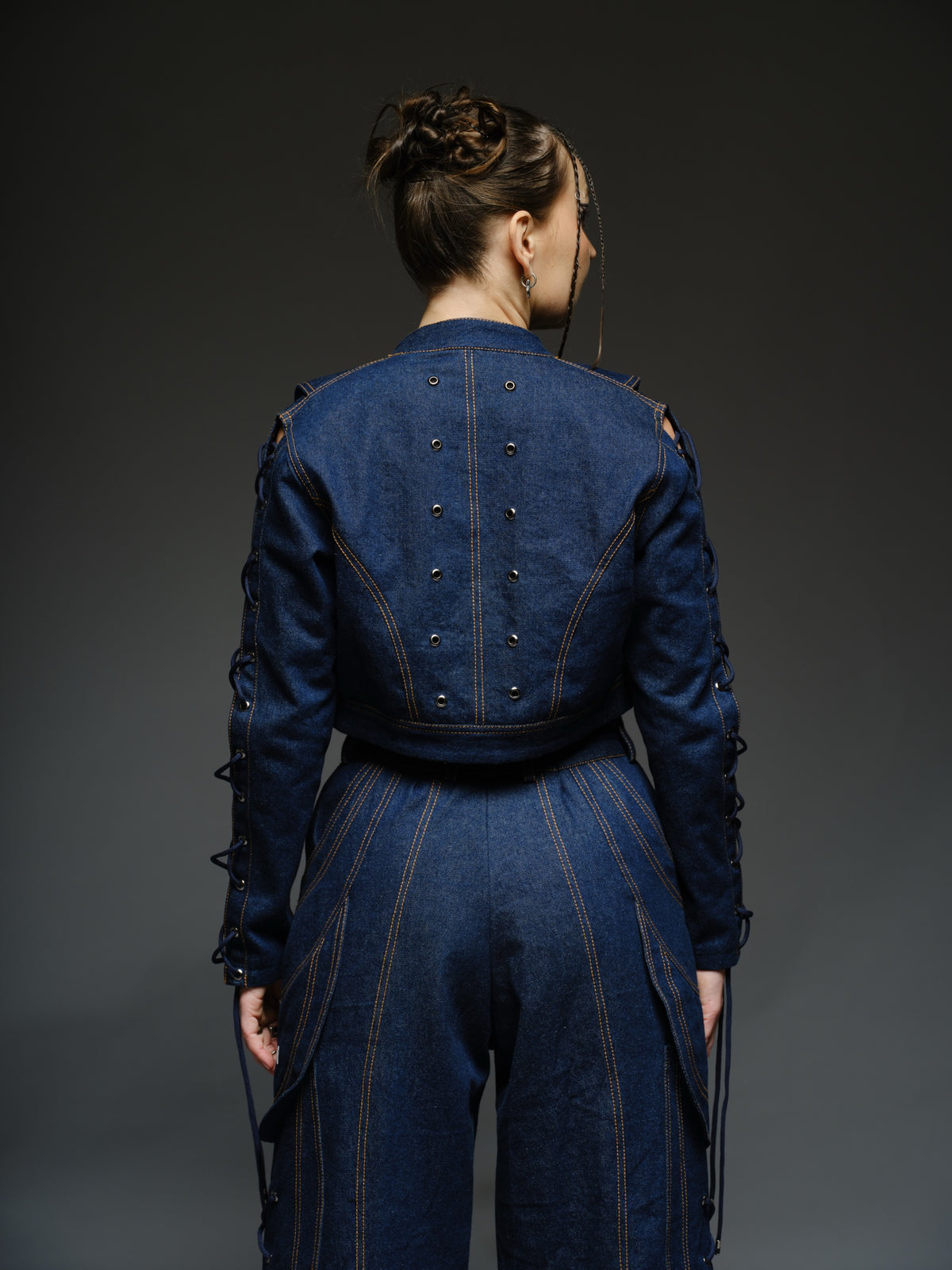 Indigo Set cropped denim jacket with oversized collar and lace-up sleeves, paired with panelled straight-leg pants with orange stitching
