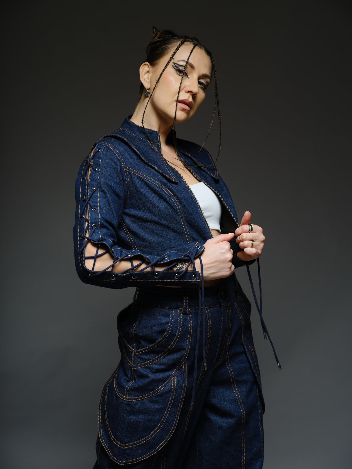 Indigo Set cropped denim jacket with oversized collar and lace-up sleeves, paired with panelled straight-leg pants with orange stitching