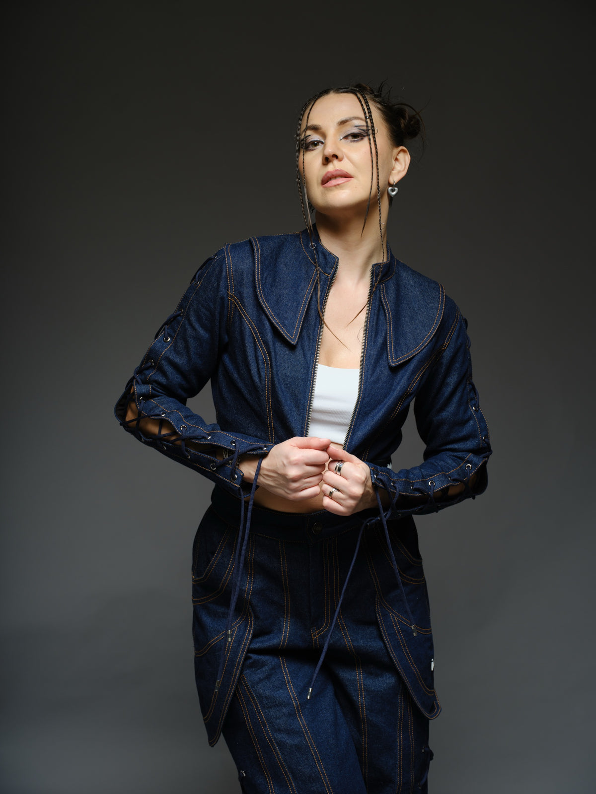 Indigo Set cropped denim jacket with oversized collar and lace-up sleeves, paired with panelled straight-leg pants with orange stitching