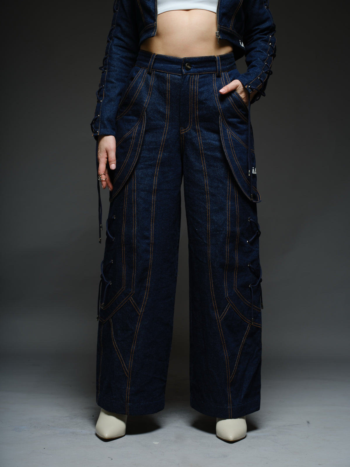 Indigo Set cropped denim jacket with oversized collar and lace-up sleeves, paired with panelled straight-leg pants with orange stitching