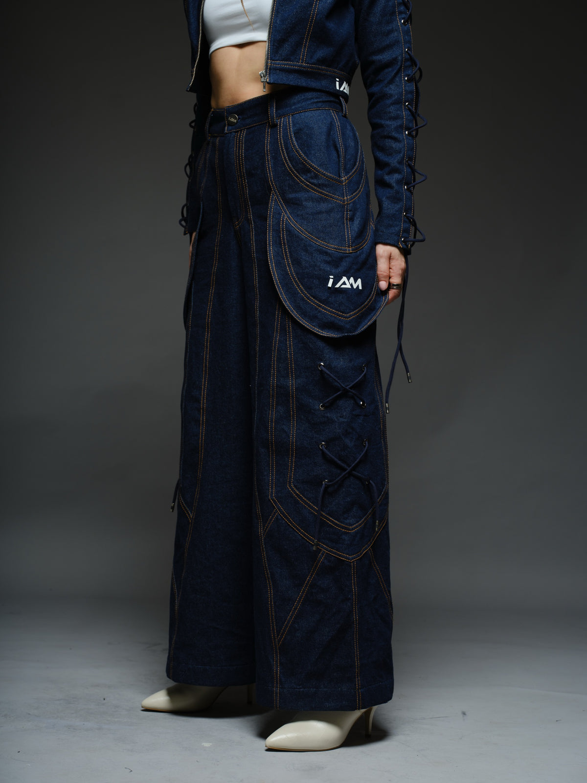 Indigo Set cropped denim jacket with oversized collar and lace-up sleeves, paired with panelled straight-leg pants with orange stitching
