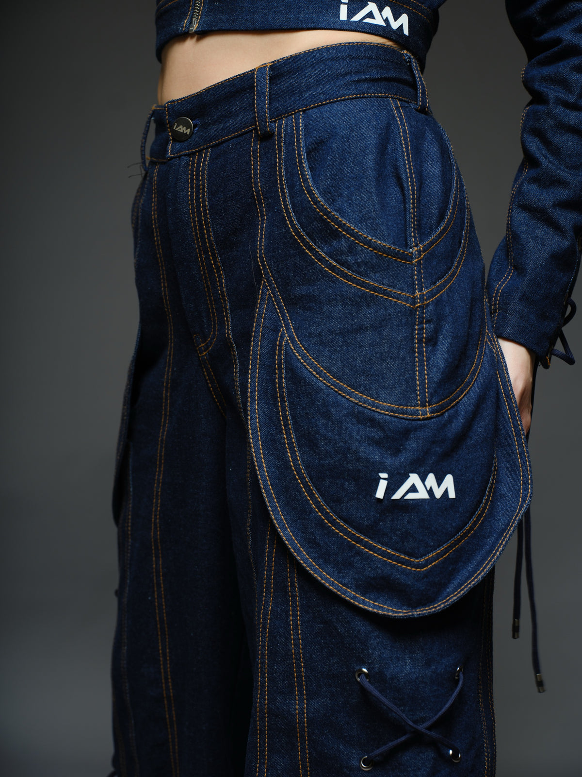 Indigo Set cropped denim jacket with oversized collar and lace-up sleeves, paired with panelled straight-leg pants with orange stitching