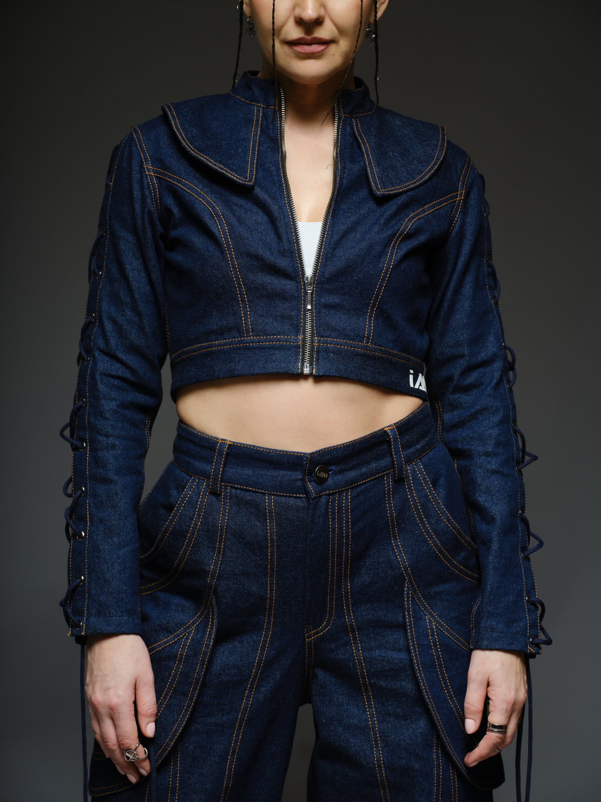 Indigo Set cropped denim jacket with oversized collar and lace-up sleeves, paired with panelled straight-leg pants with orange stitching