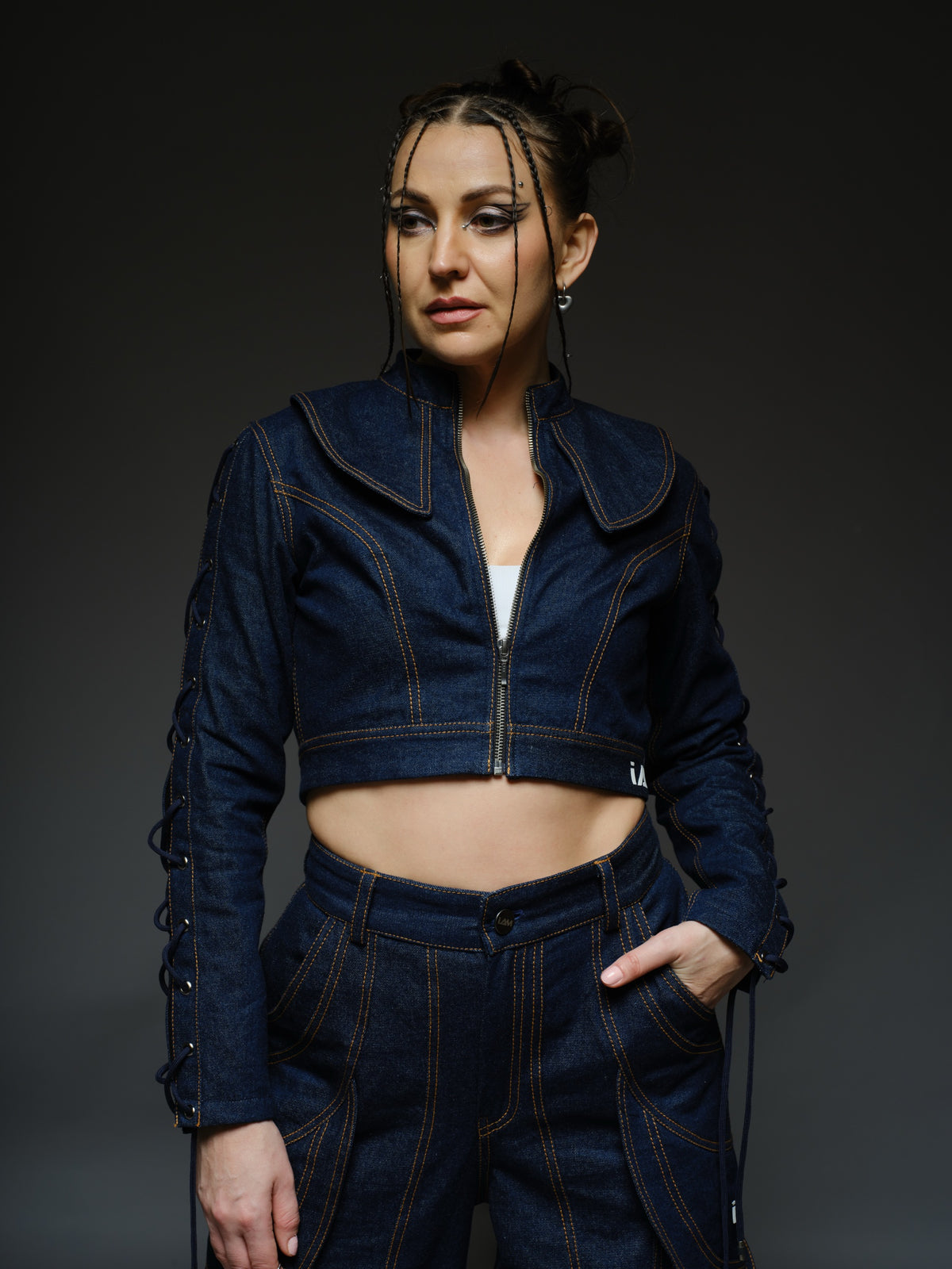 Indigo Set cropped denim jacket with oversized collar and lace-up sleeves, paired with panelled straight-leg pants with orange stitching