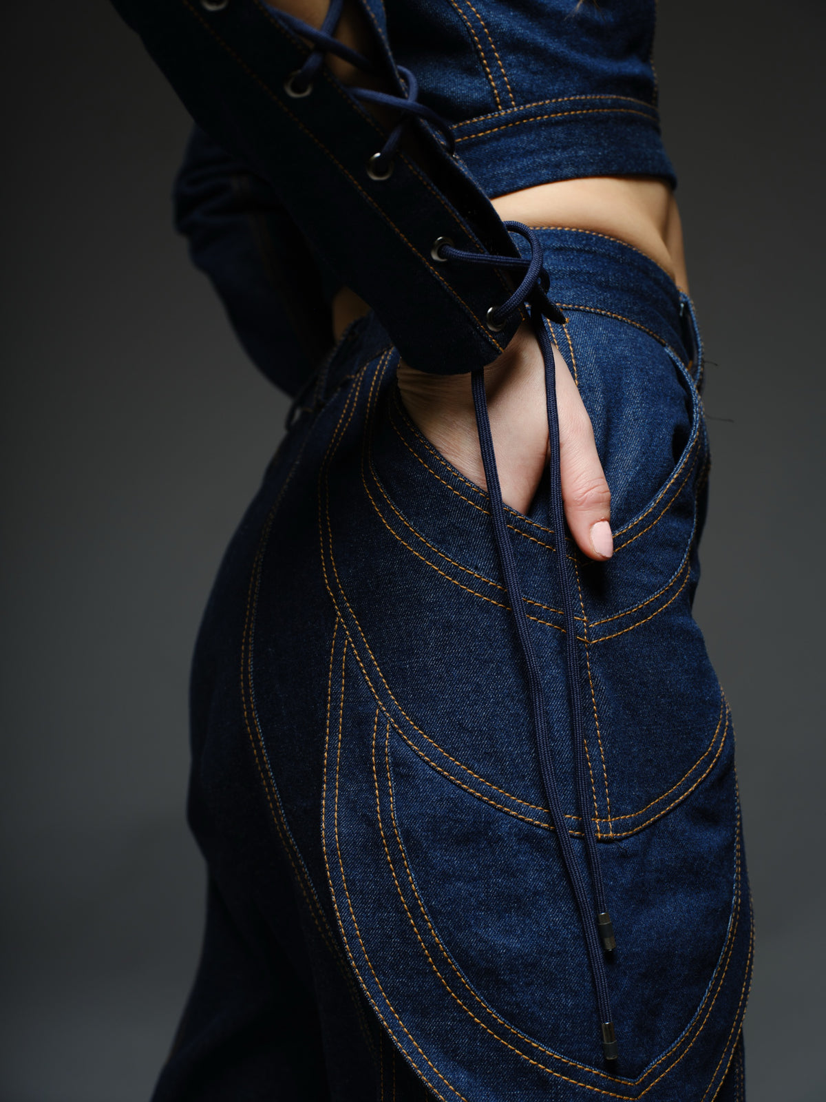 Indigo Set cropped denim jacket with oversized collar and lace-up sleeves, paired with panelled straight-leg pants with orange stitching