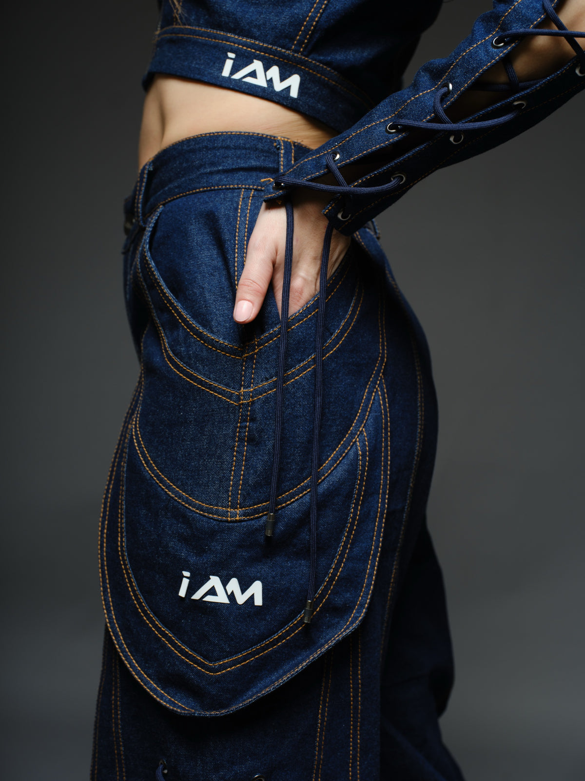 Indigo Set cropped denim jacket with oversized collar and lace-up sleeves, paired with panelled straight-leg pants with orange stitching