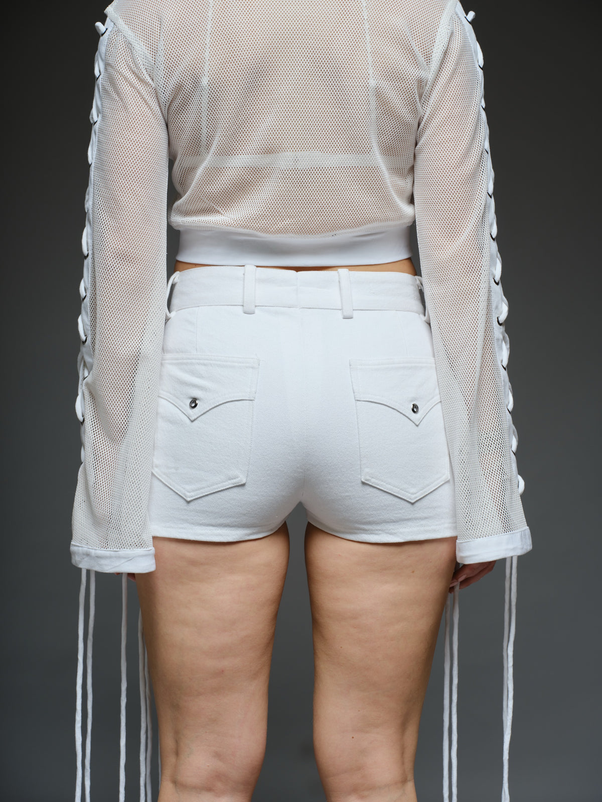 White net cropped top with front and sleeve lacing, paired with a white denim wrap mini skort with cords and metallic details
