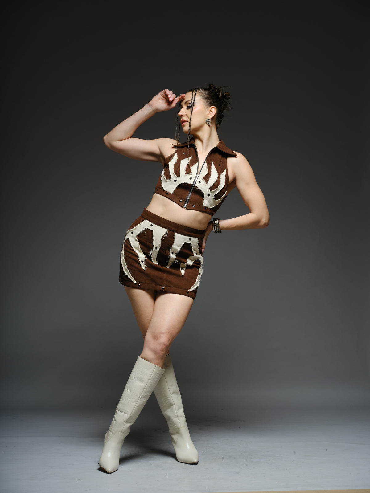 Brown suede collared crop top and mini skirt with angular white drill patches, frayed edges and silver-tone metal eyelets
