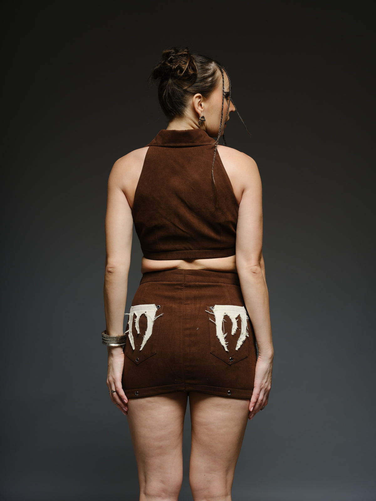 Brown suede collared crop top and mini skirt with angular white drill patches, frayed edges and silver-tone metal eyelets