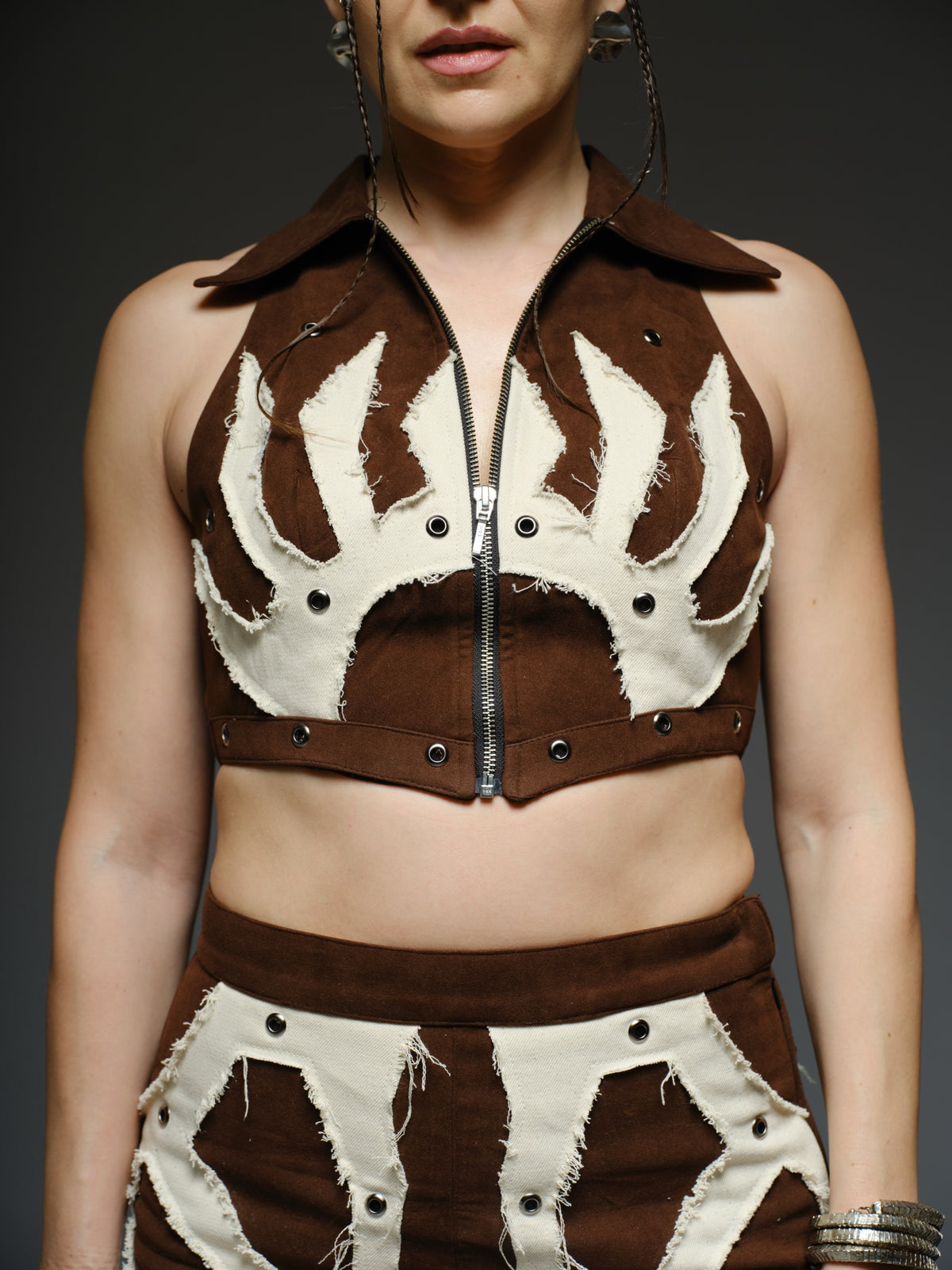 Brown suede collared crop top and mini skirt with angular white drill patches, frayed edges and silver-tone metal eyelets