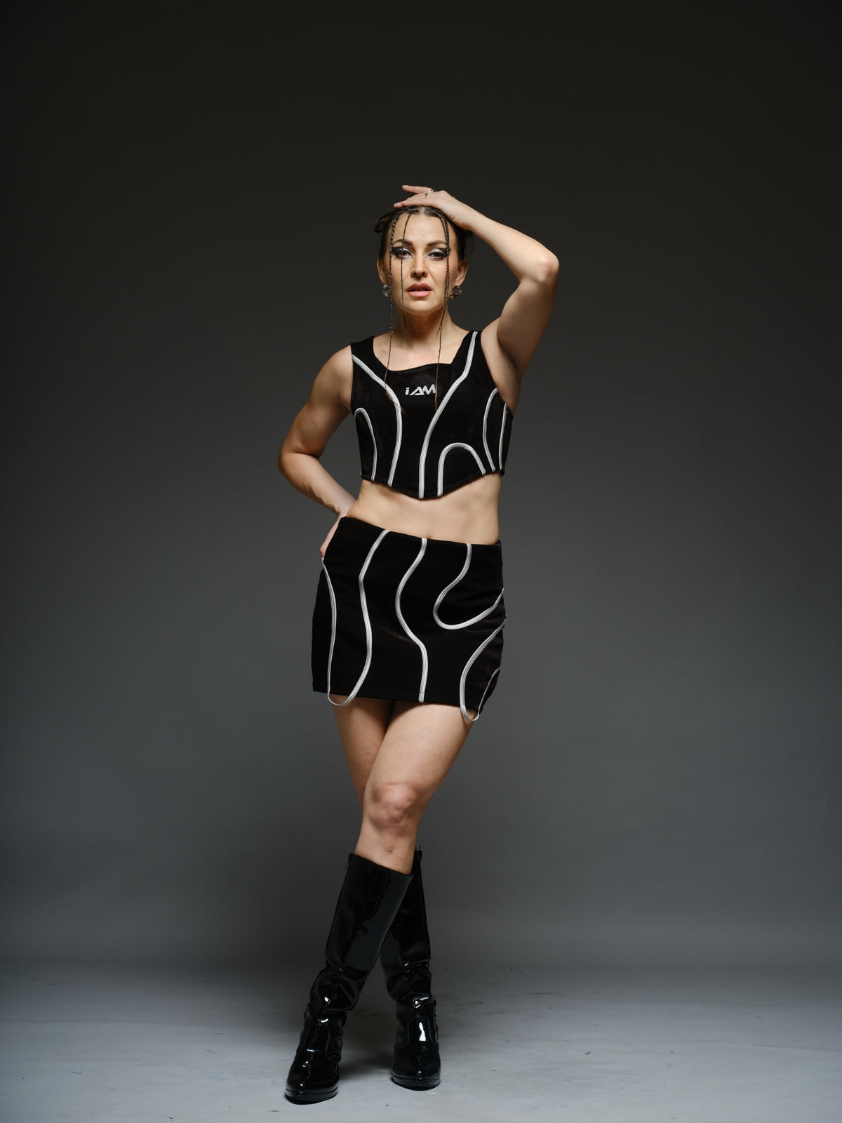 Black crop top and mini skirt with light-coloured curved cord detailing and loops extending below the skirt hem
