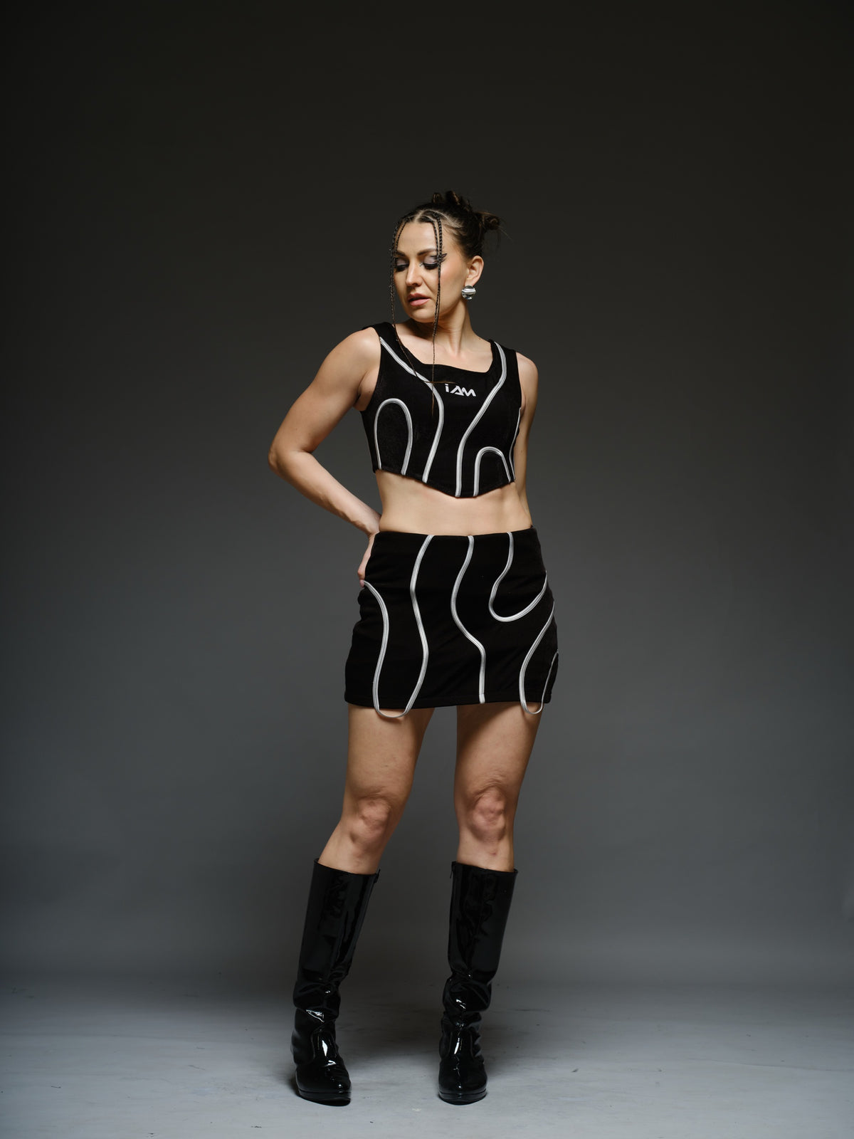 Black crop top and mini skirt with light-coloured curved cord detailing and loops extending below the skirt hem