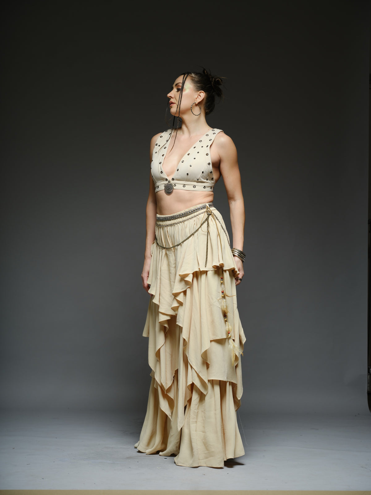 Beige studded V-neck bralette with a central brooch, paired with layered ruffle palazzo trousers with metallic belt and chain details