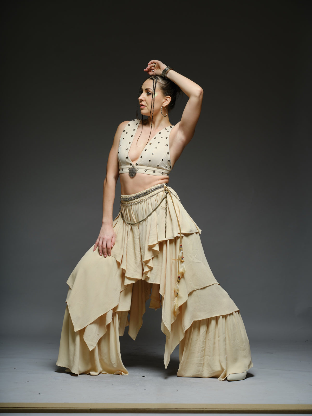 Beige studded V-neck bralette with a central brooch, paired with layered ruffle palazzo trousers with metallic belt and chain details
