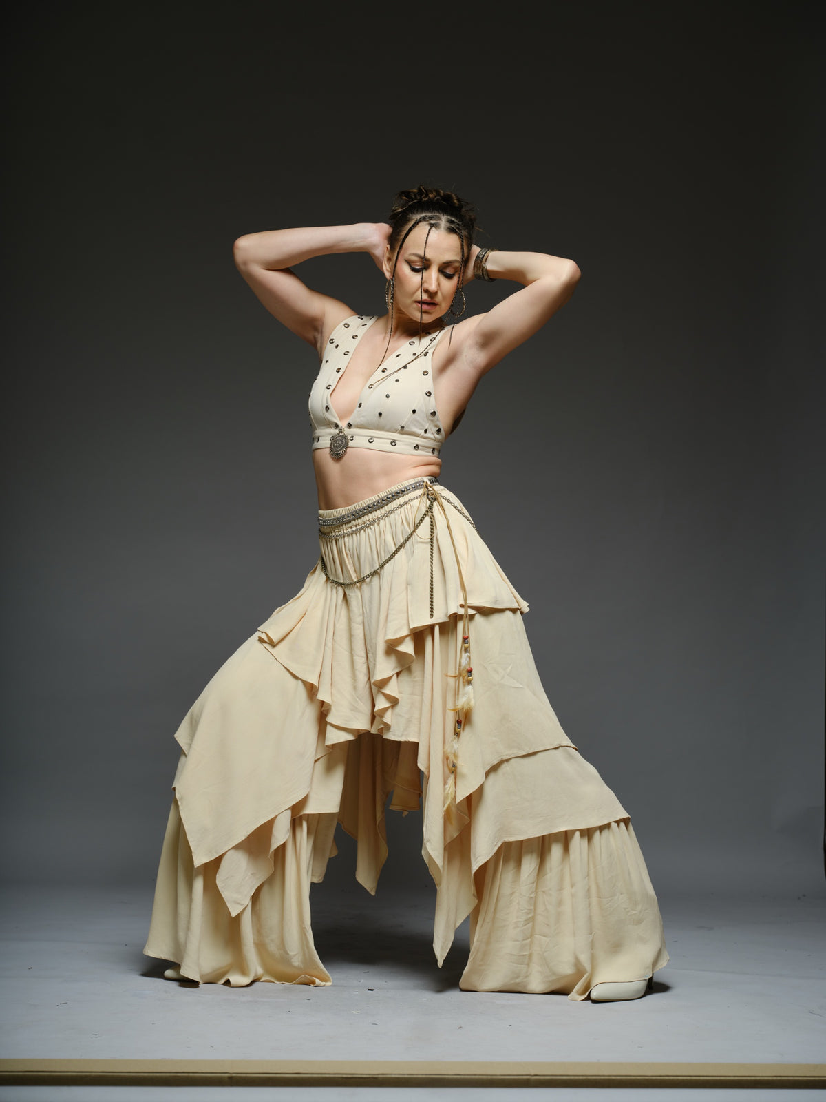 Beige studded V-neck bralette with a central brooch, paired with layered ruffle palazzo trousers with metallic belt and chain details