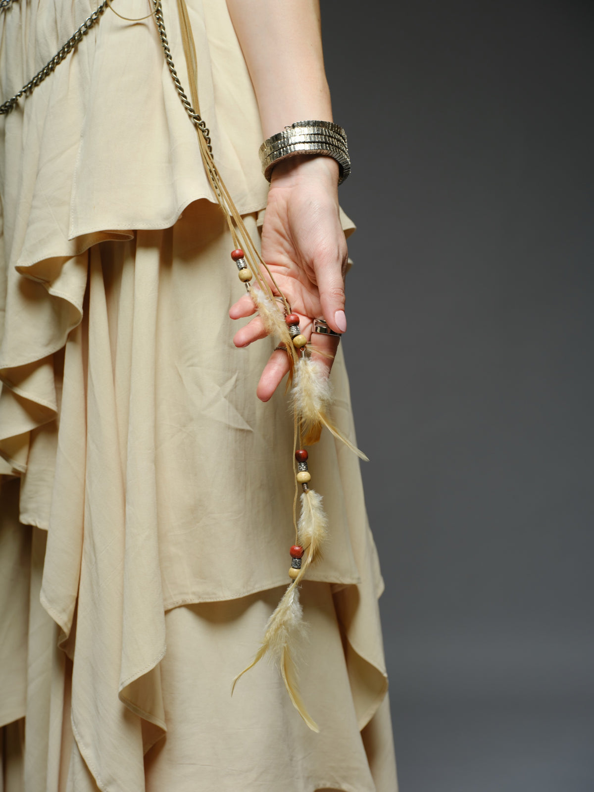 Beige studded V-neck bralette with a central brooch, paired with layered ruffle palazzo trousers with metallic belt and chain details