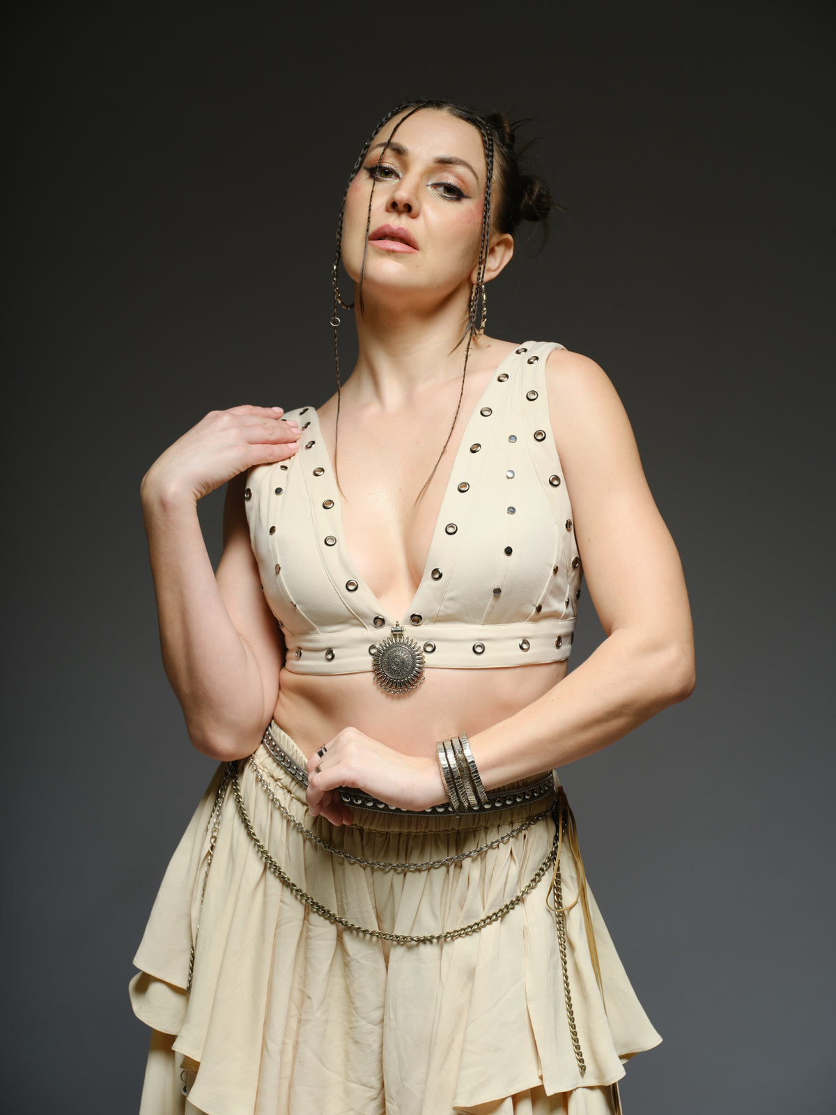 Beige studded V-neck bralette with a central brooch, paired with layered ruffle palazzo trousers with metallic belt and chain details