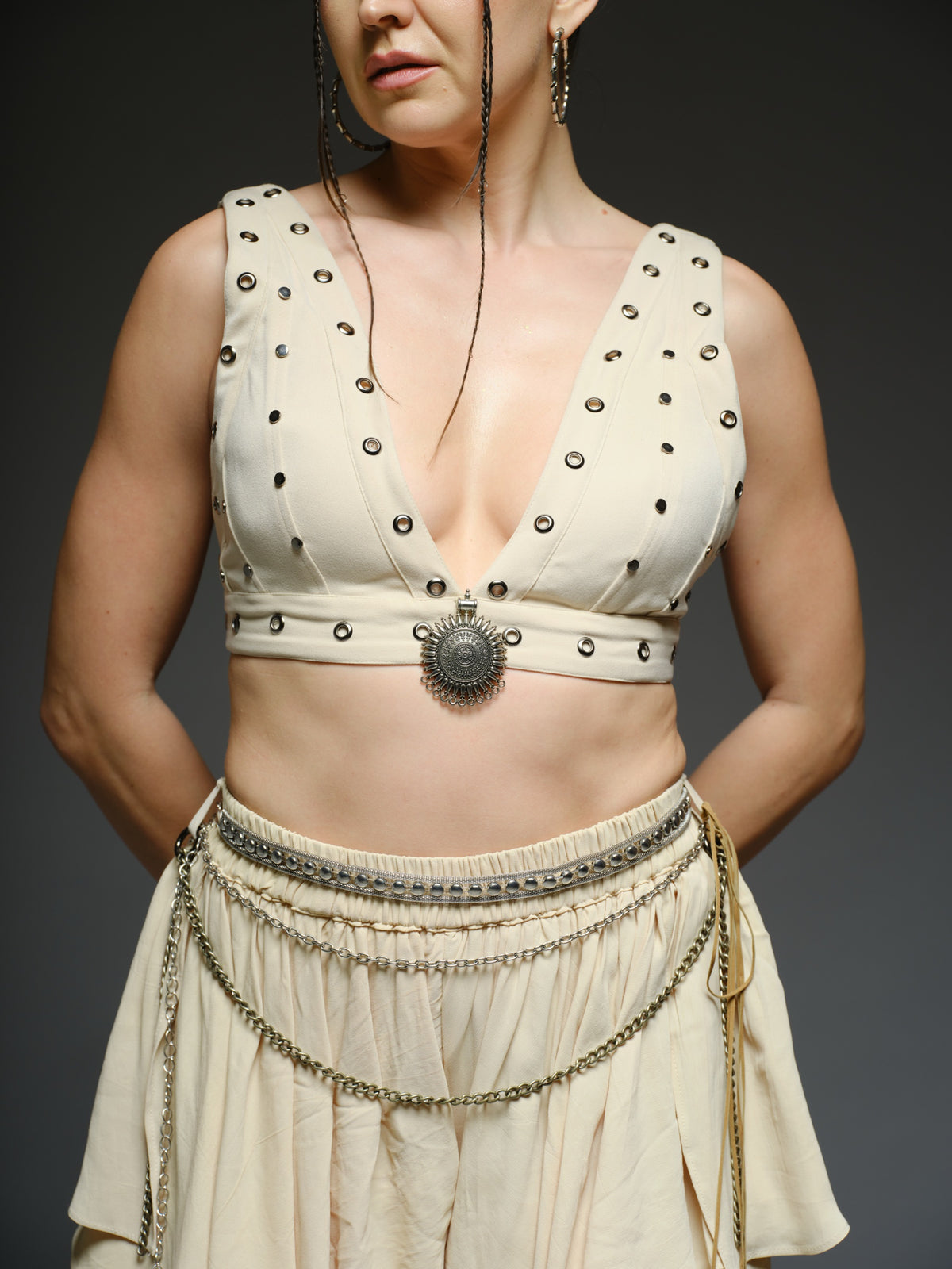 Beige studded V-neck bralette with a central brooch, paired with layered ruffle palazzo trousers with metallic belt and chain details
