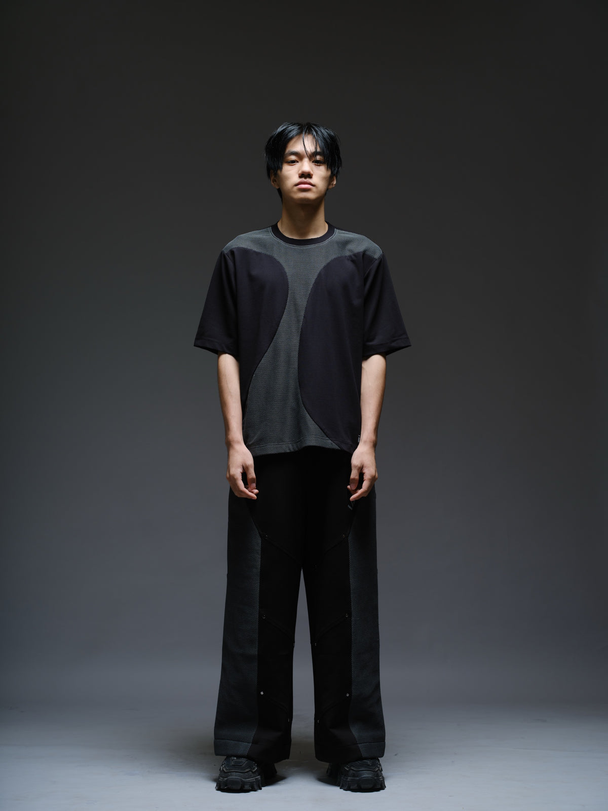 Loose black wide-leg trousers with grey net side panels and small silver-tone studs at the panel corners