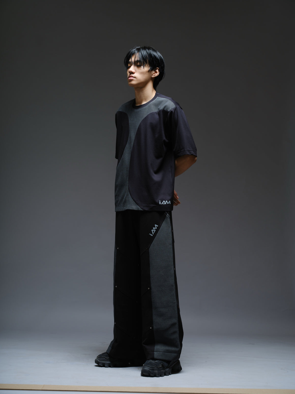 Loose black wide-leg trousers with grey net side panels and small silver-tone studs at the panel corners