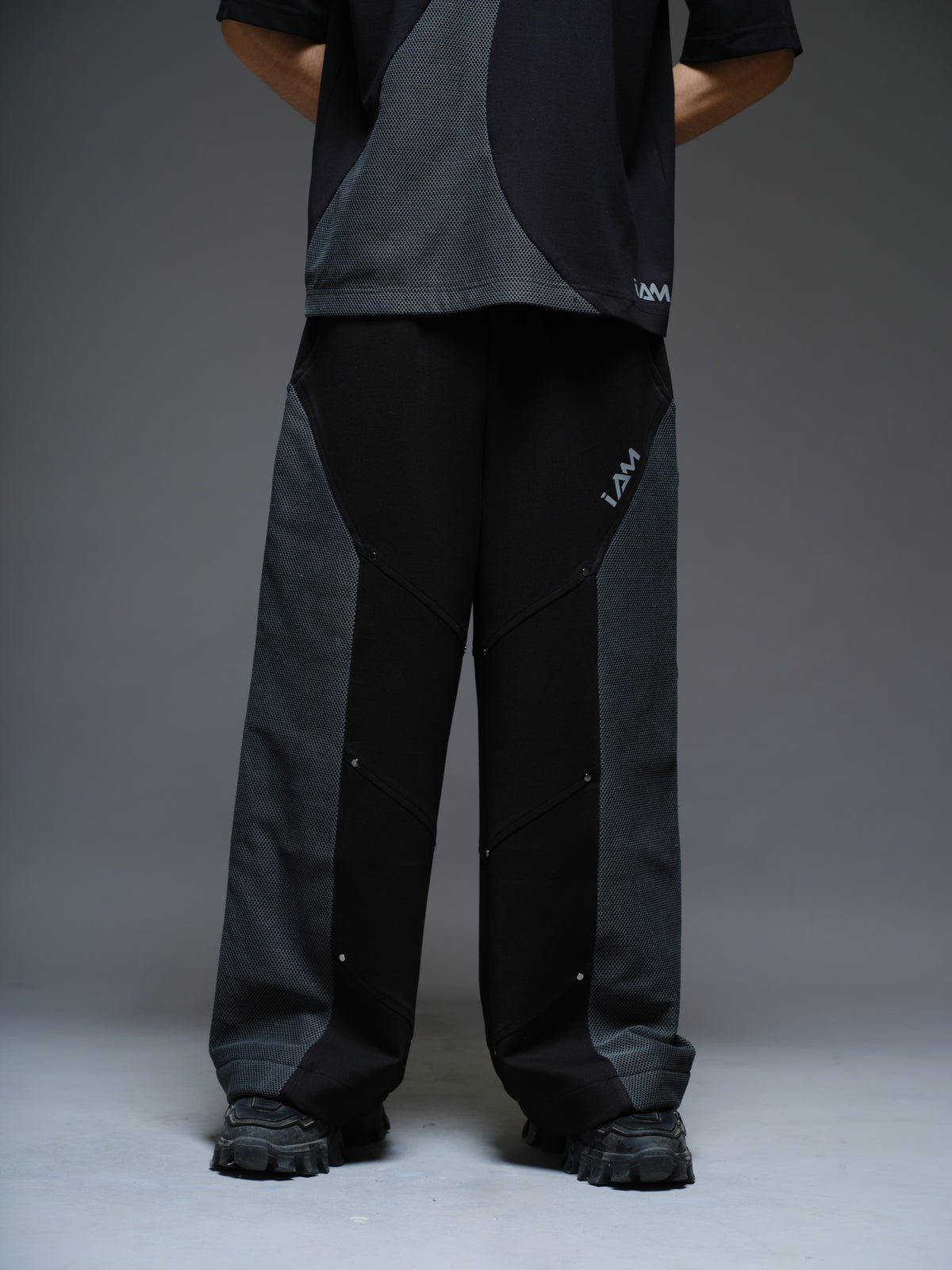 Loose black wide-leg trousers with grey net side panels and small silver-tone studs at the panel corners