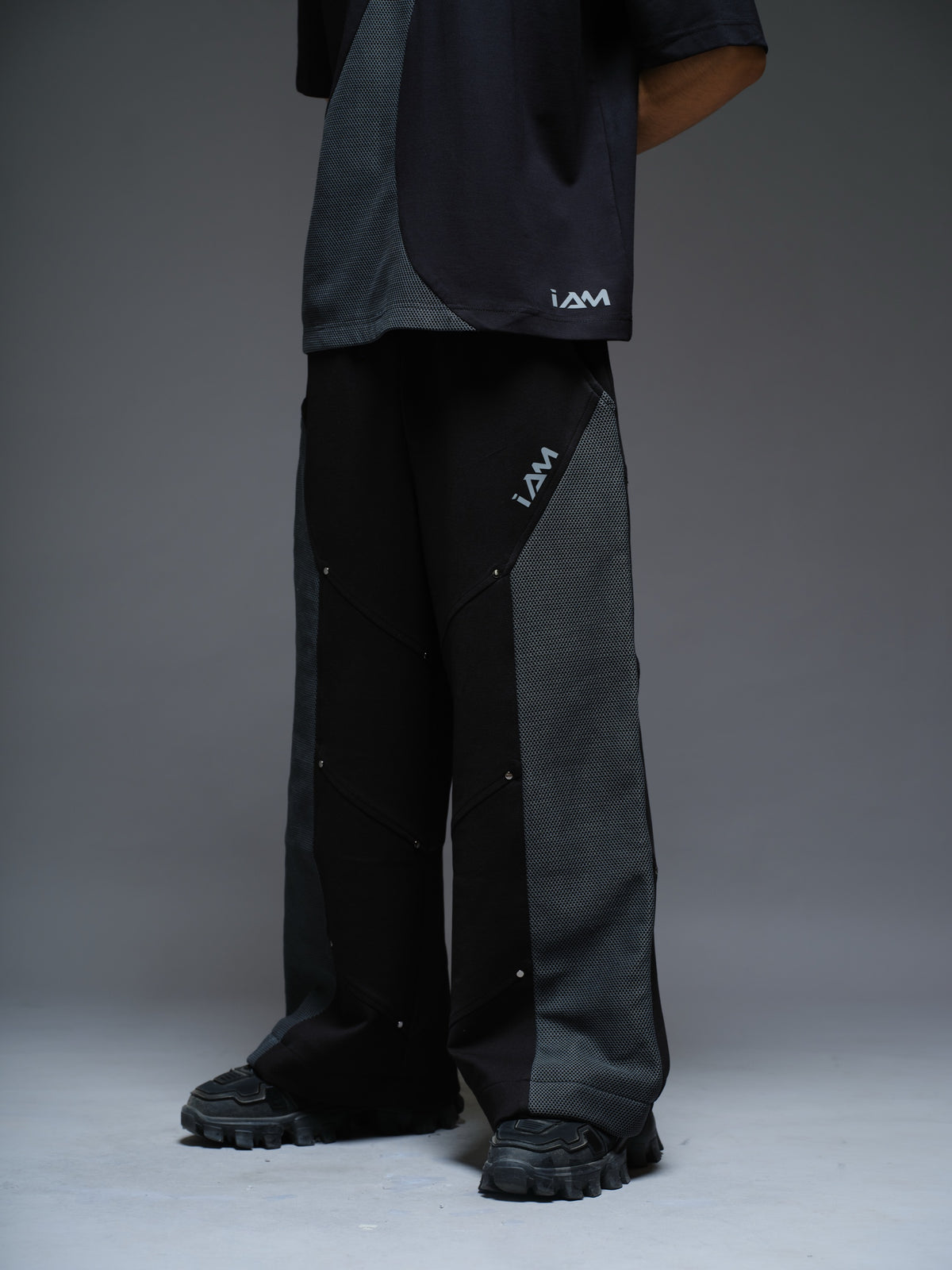Loose black wide-leg trousers with grey net side panels and small silver-tone studs at the panel corners