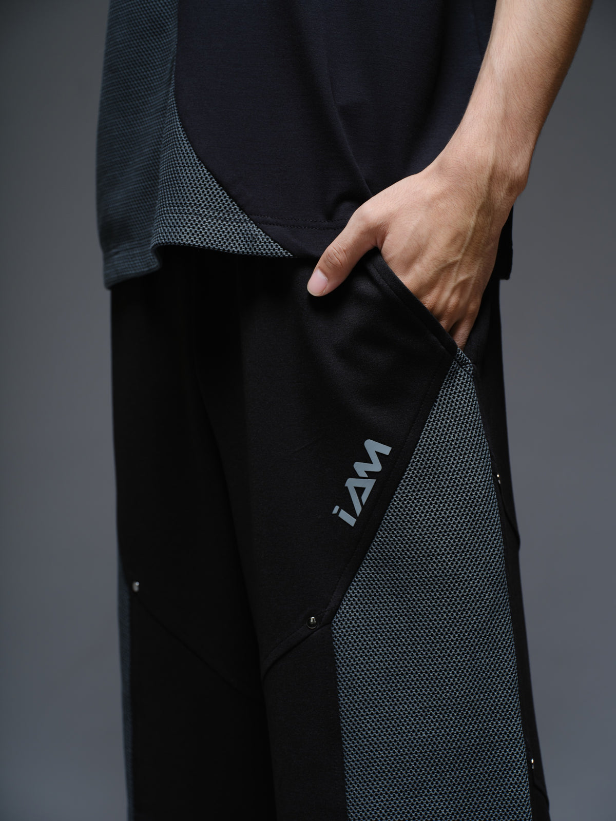 Loose black wide-leg trousers with grey net side panels and small silver-tone studs at the panel corners
