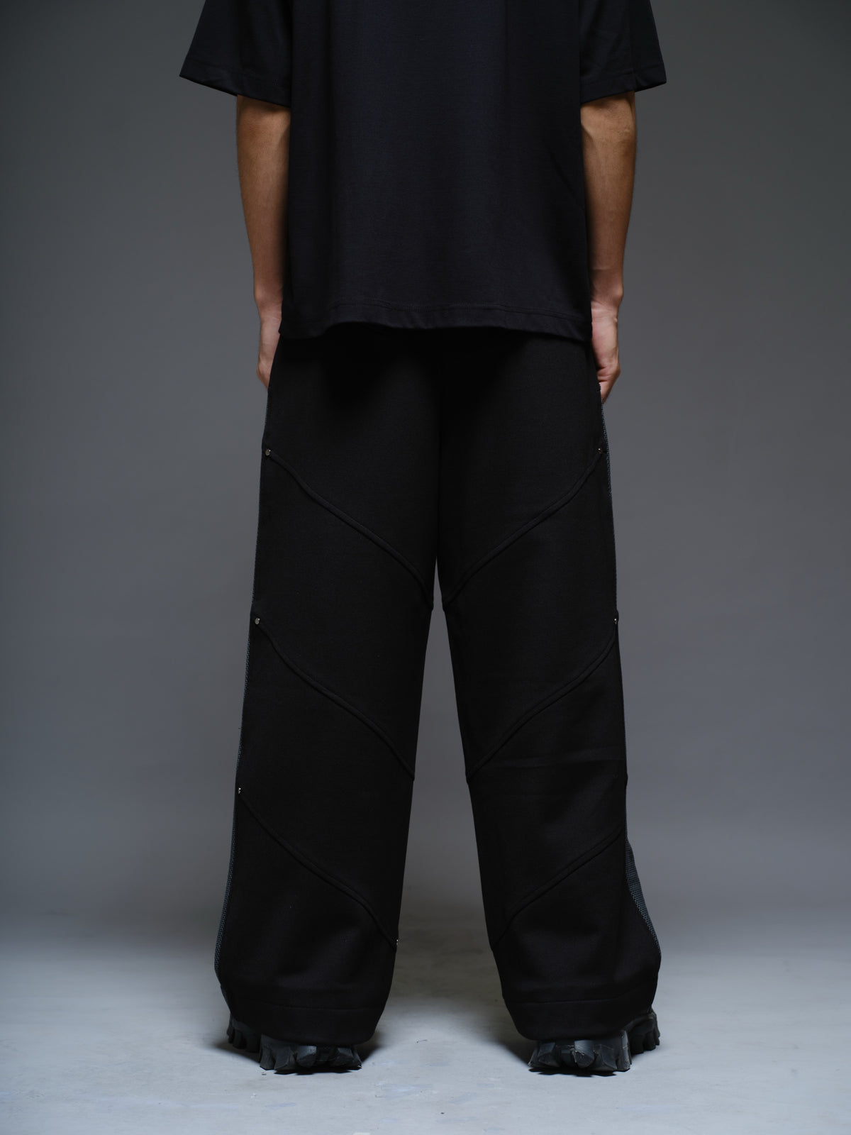 Loose black wide-leg trousers with grey net side panels and small silver-tone studs at the panel corners