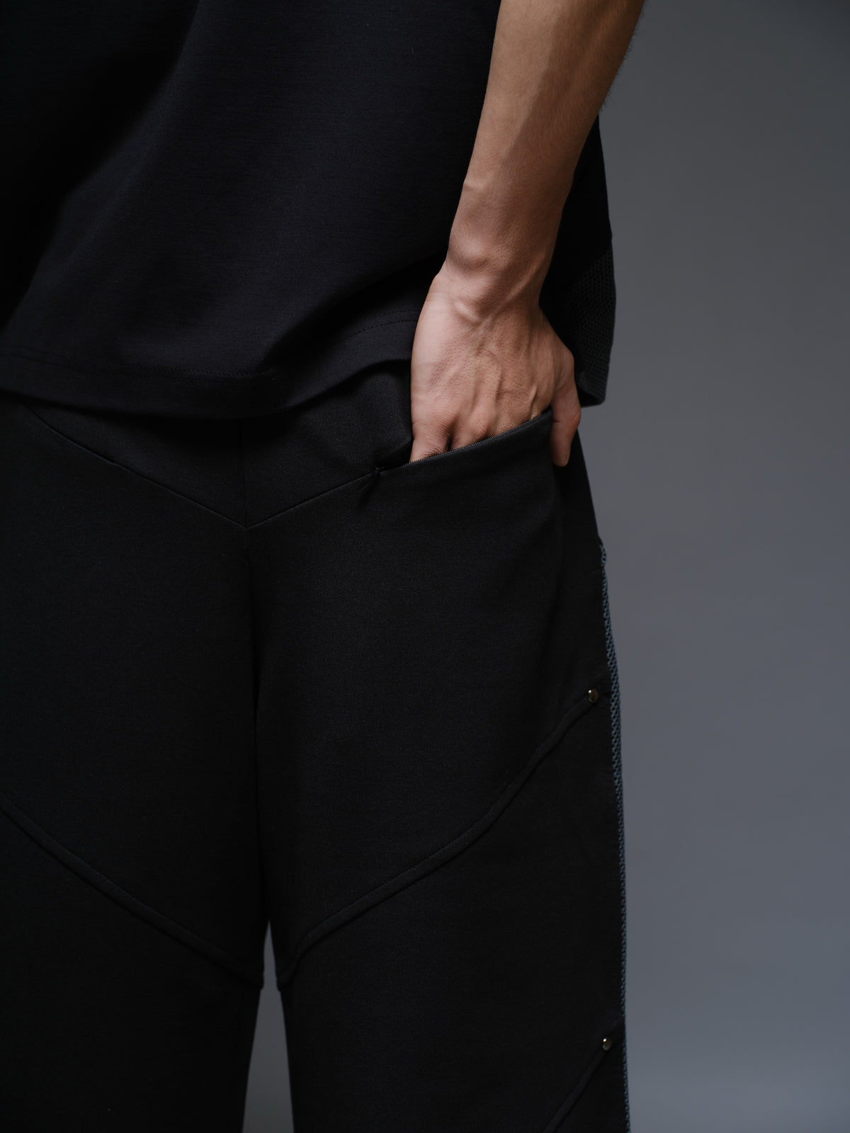 Loose black wide-leg trousers with grey net side panels and small silver-tone studs at the panel corners