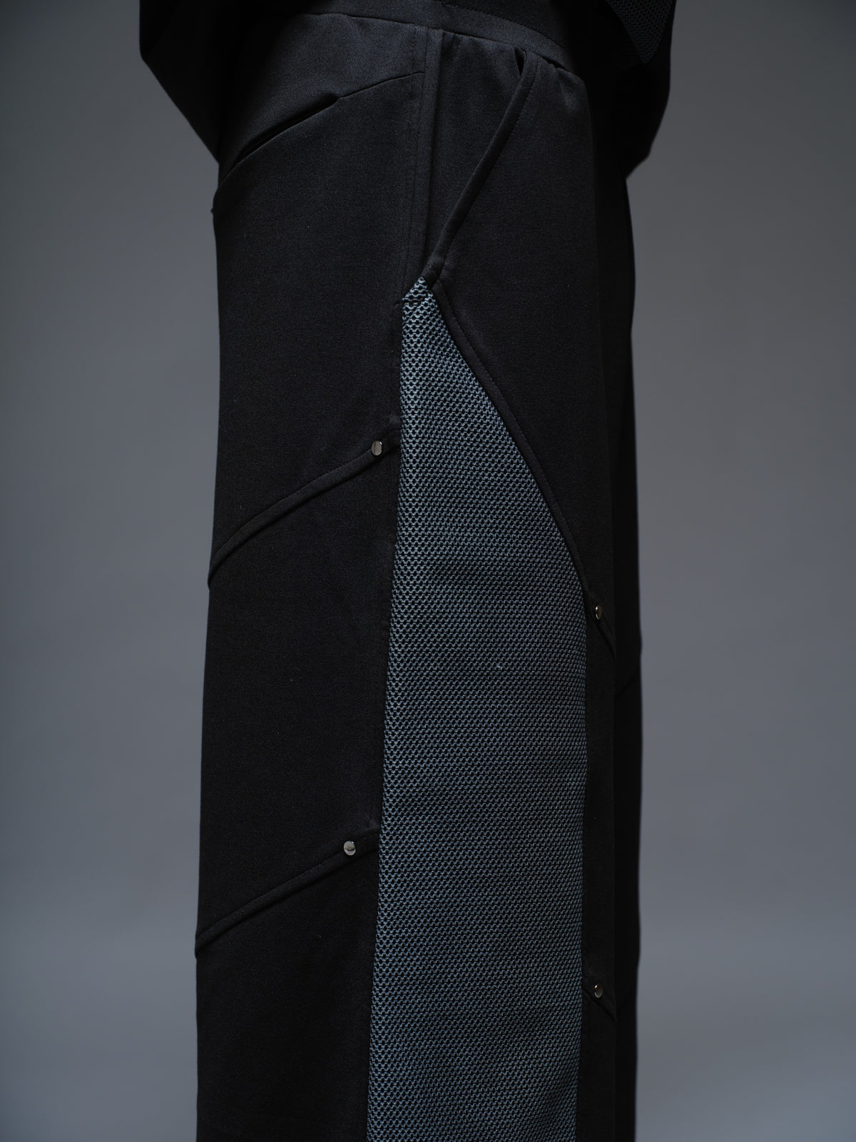 Loose black wide-leg trousers with grey net side panels and small silver-tone studs at the panel corners